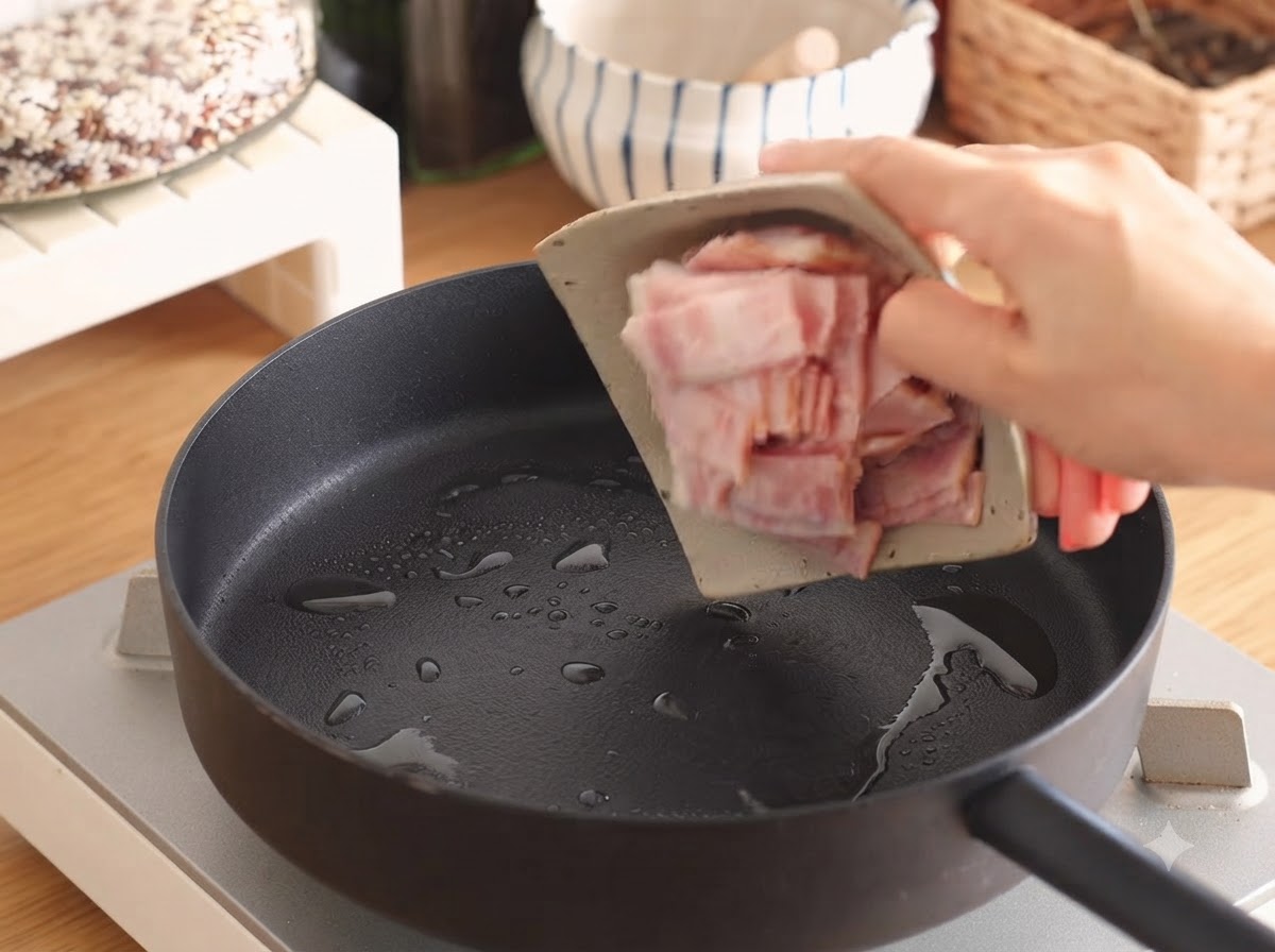 Bacon strips sizzling in a frying pan with a small amount of oil.