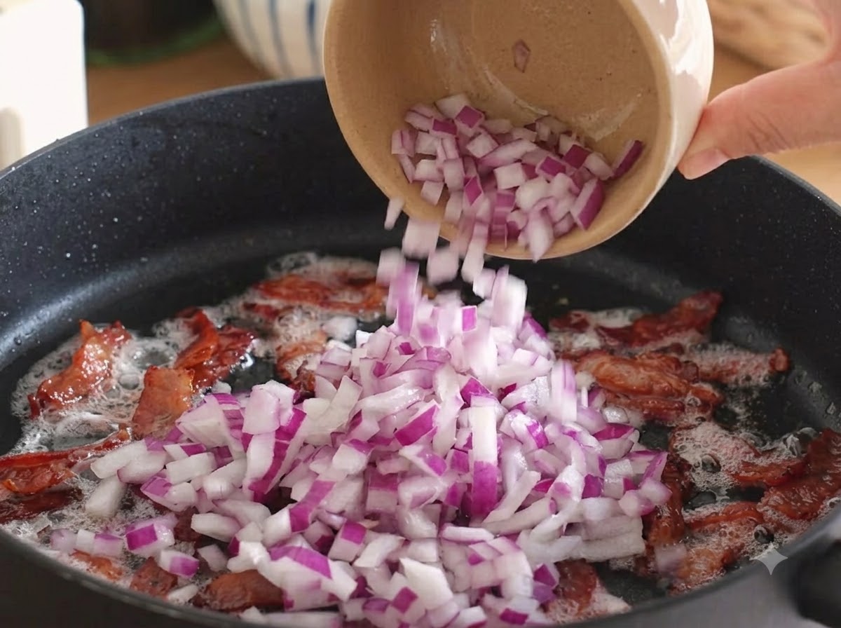 Diced red onions being poured into the pan over the cooked bacon.