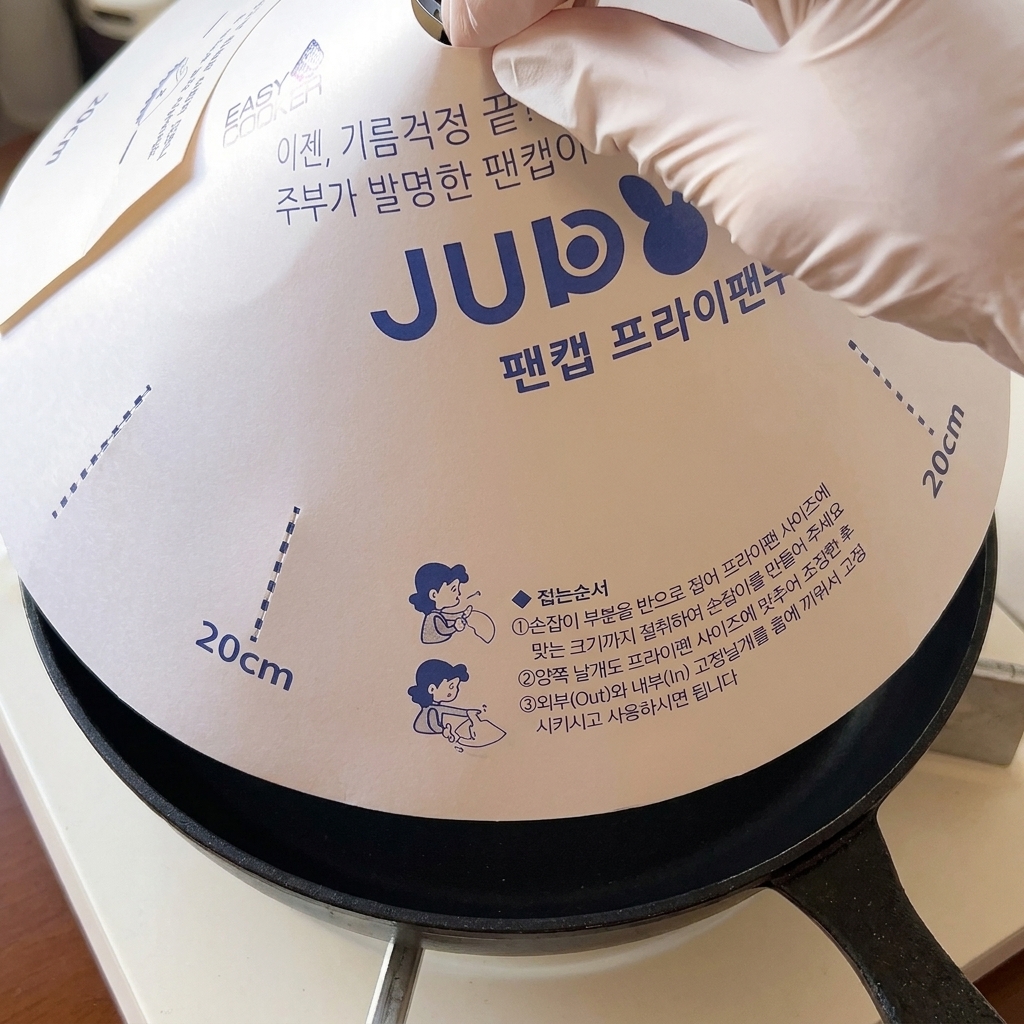 A white paper lid being placed over a skillet to melt cheese on hamburger patties.
