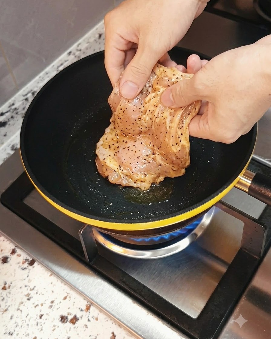 Marinated chicken breast being placed into a hot frying pan with a gas flame underneath.