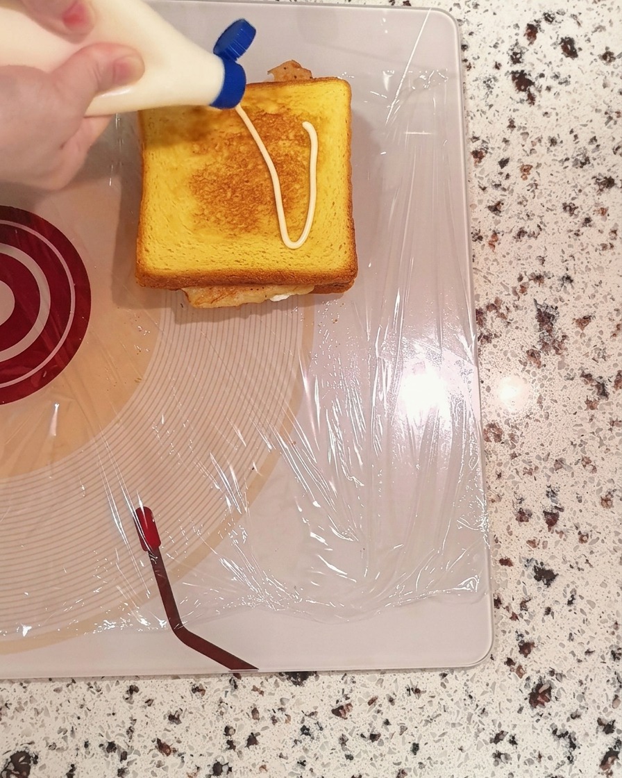 Mayonnaise being squeezed from a bottle onto a slice of toasted bread.