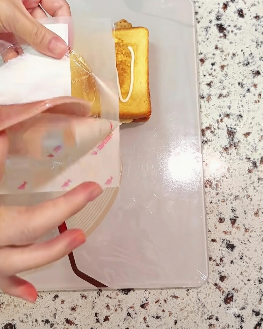 A slice of ham being layered onto the assembling sandwich bread.