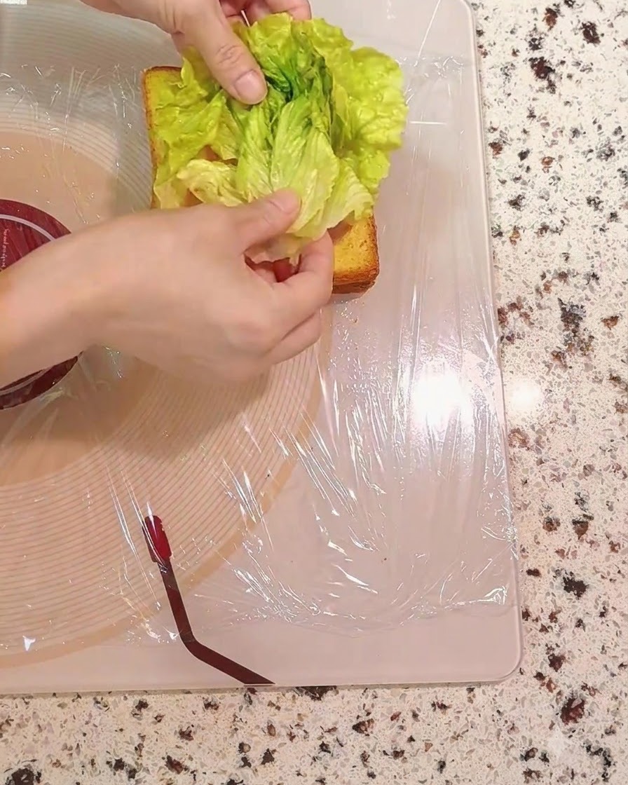 Fresh green lettuce leaves being placed onto the sandwich layers.