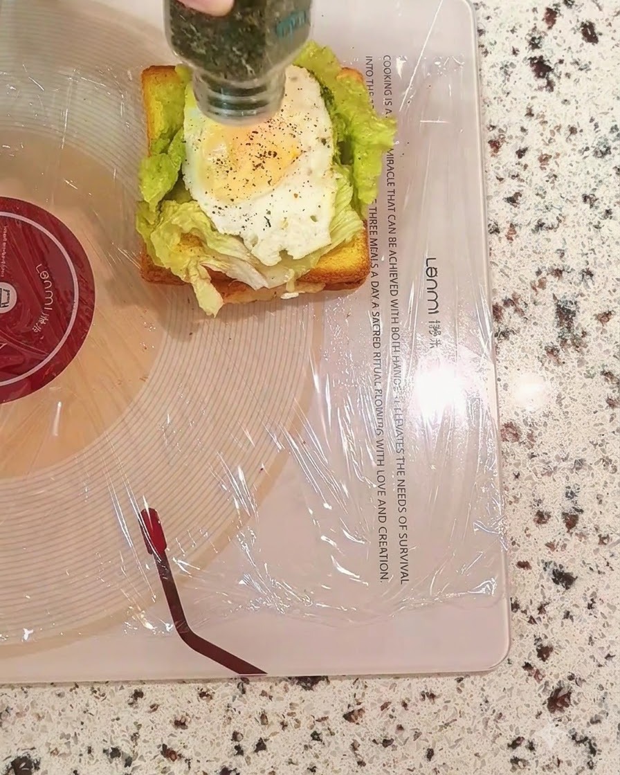 Sprinkling dried parsley from a bottle onto the egg layer of the sandwich.