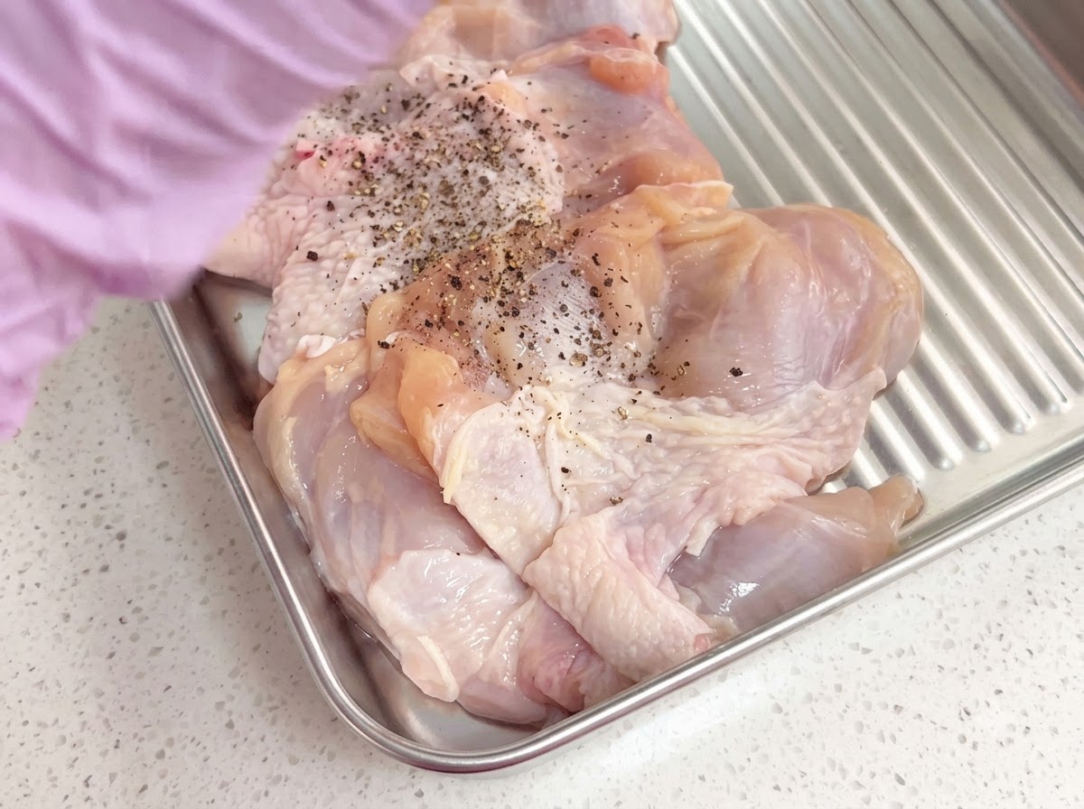 Debone chicken thighs seasoned with freshly ground black pepper inside a metal tray.