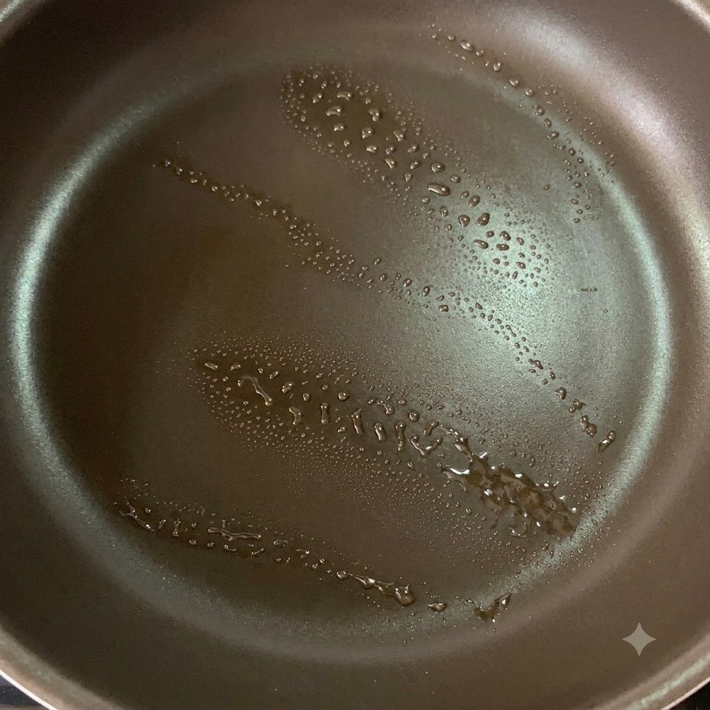A non-stick pan with a light spray of oil prepared for searing chicken thighs.