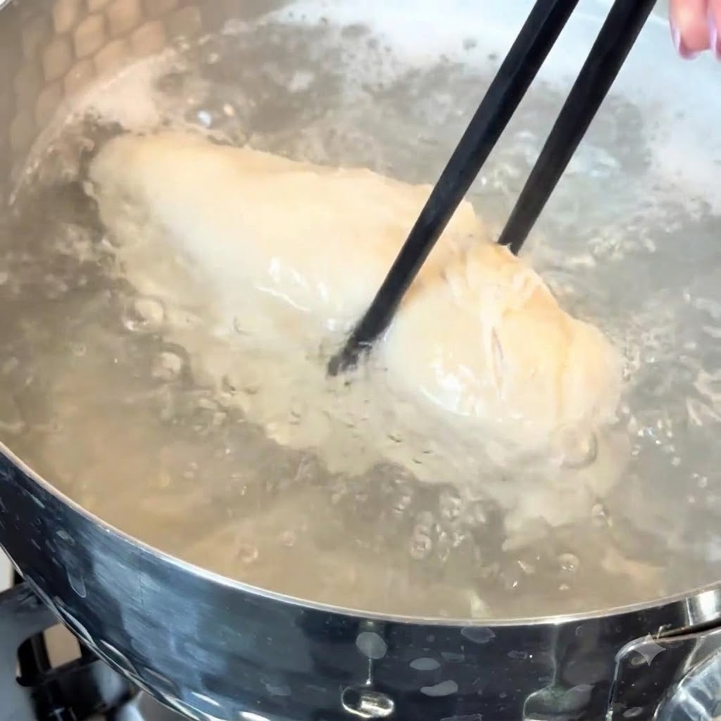 A chicken breast simmering in hot water inside a cooking pot.