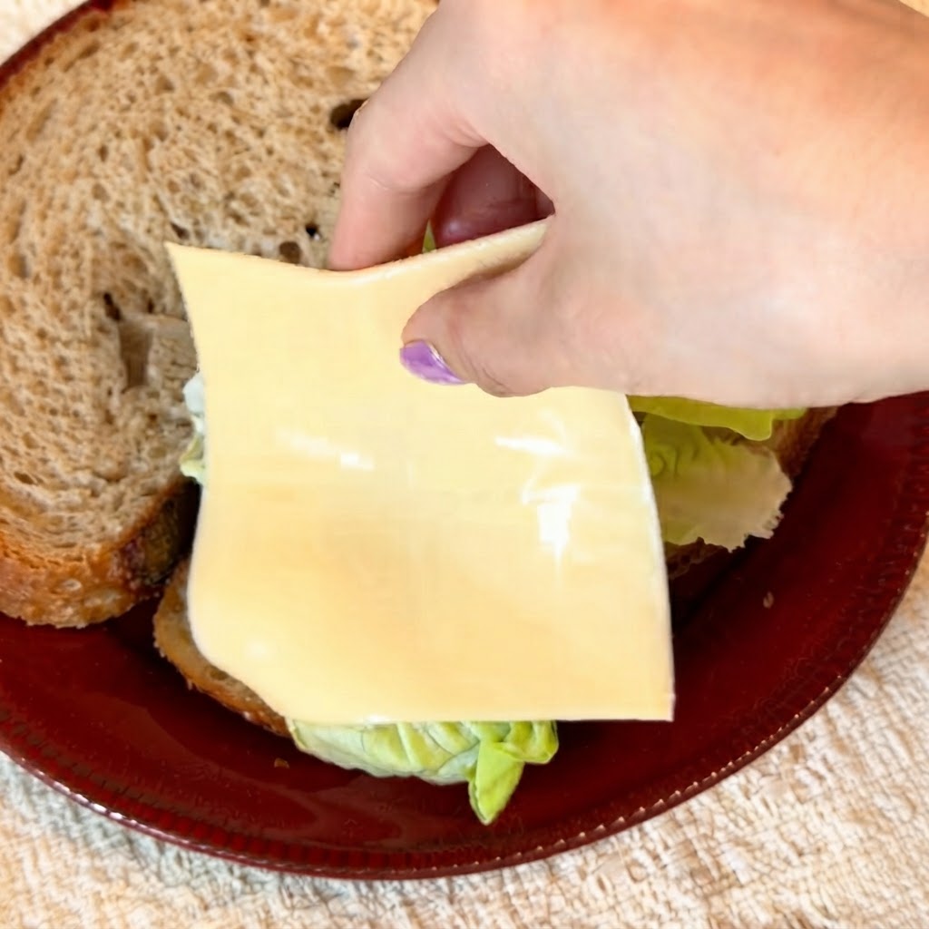 Two slices of yellow reduced-fat cheese being carefully laid over crisp green lettuce.