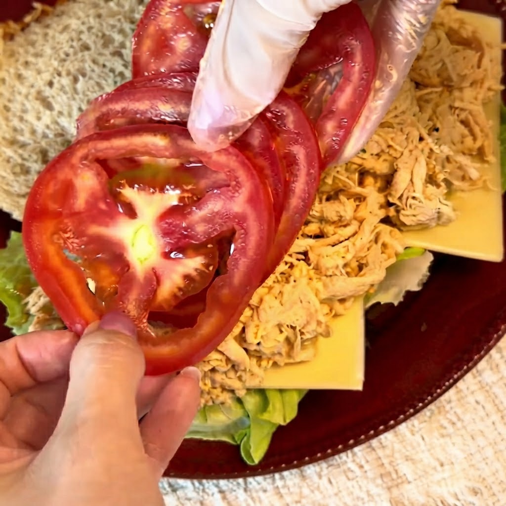 Fresh red tomato slices being neatly arranged over the shredded chicken filling.