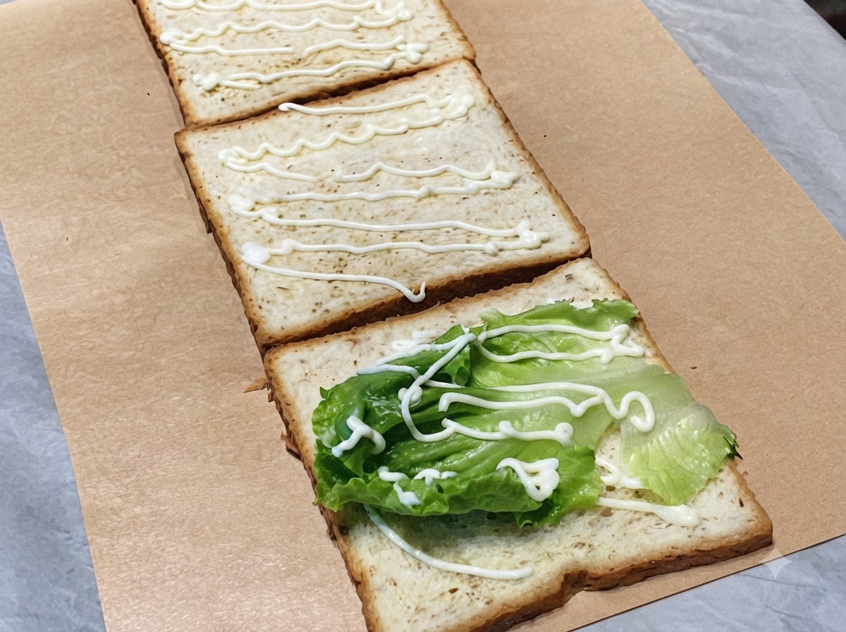 Slices of fresh green cucumber arranged on the second slice of toast with a drizzle of mayonnaise.