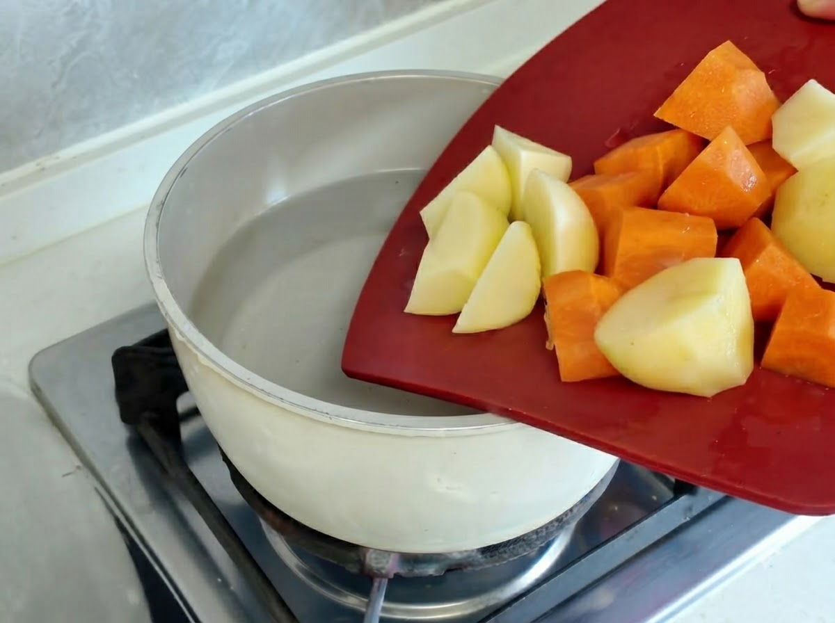 Potatoes and carrot pieces boiling inside a pot on a hot stove burner.