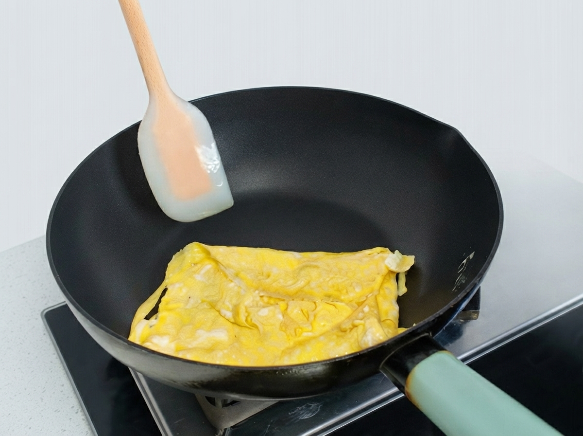 Partially folded egg omelette in a frying pan being shaped with a silicone spatula.