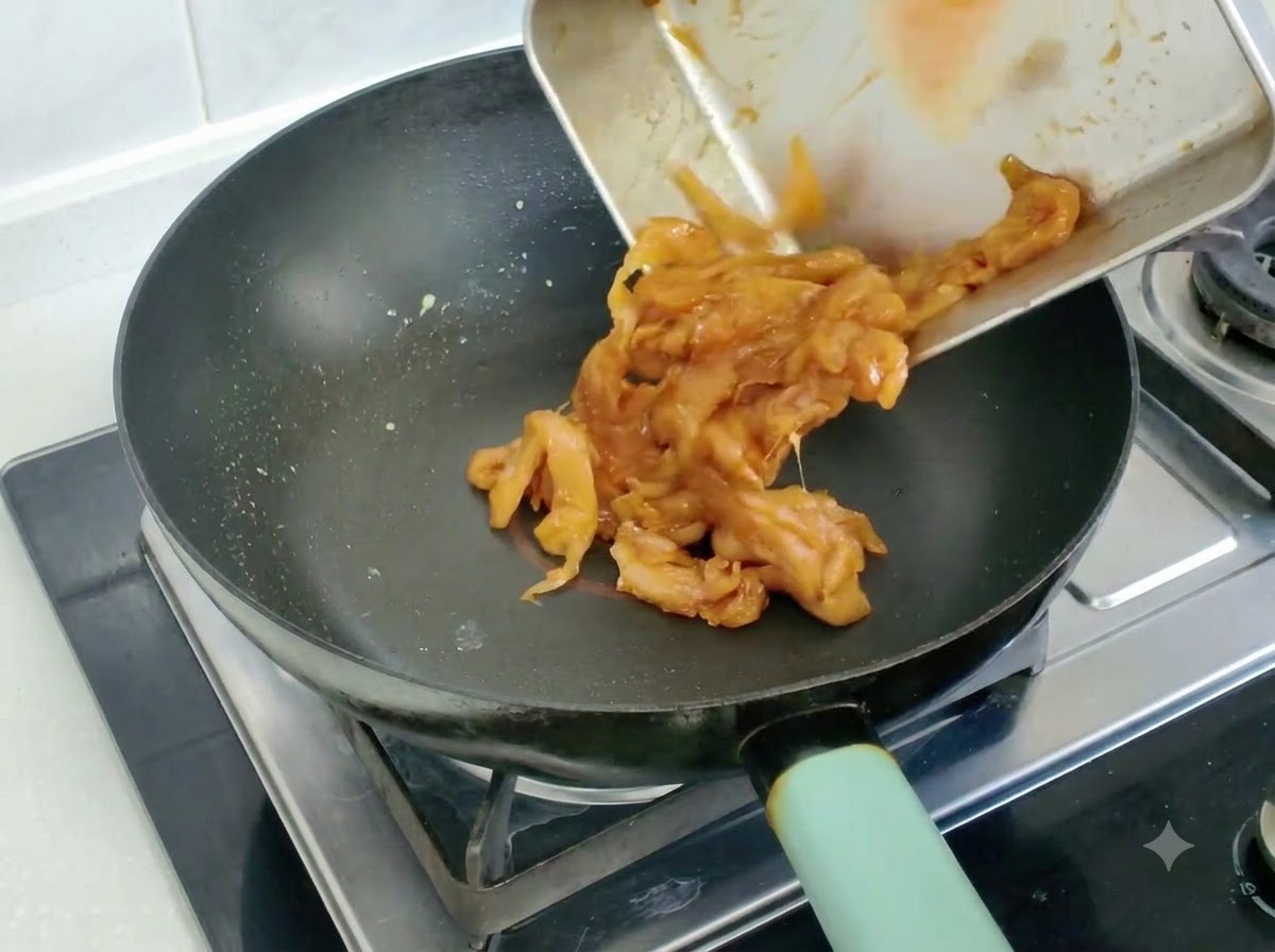 Marinated chicken slices being emptied and stir-fried in a frying pan.