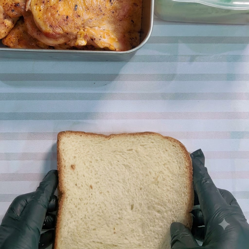 A serrated knife slicing through a wrapped sandwich diagonally on a striped surface.