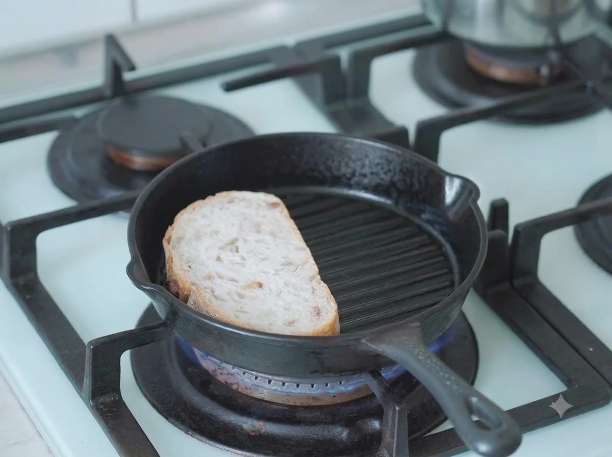 A slice of sourdough bread toasting in a hot cast-iron grill pan on the stove.