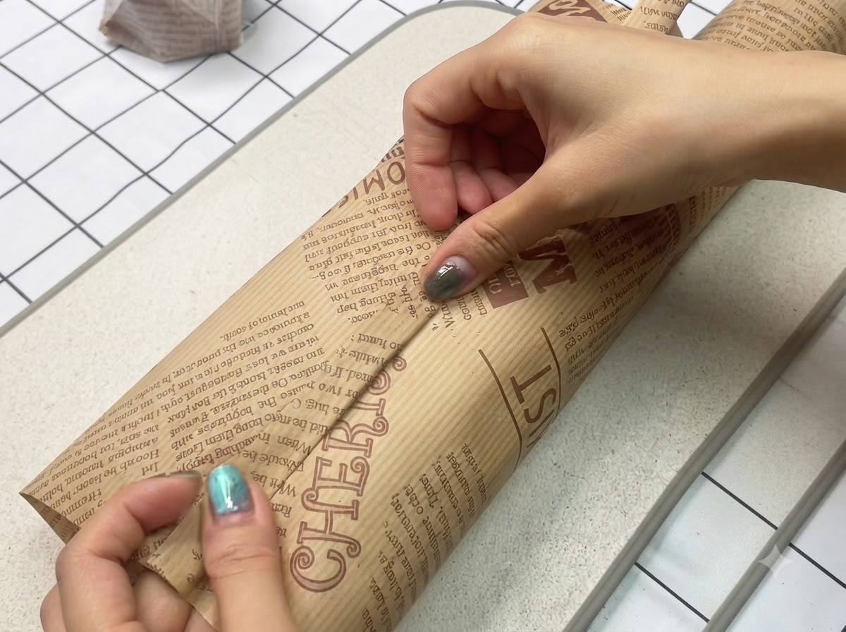 A freshly made sandwich being wrapped tightly and securely in decorative brown parchment paper.