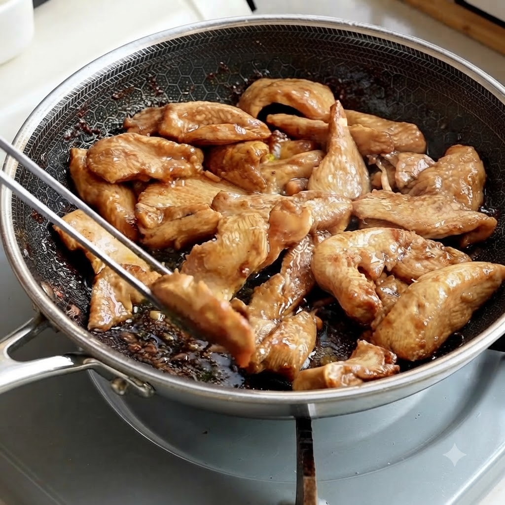 Metal tongs picking up cooked chicken strips from a pan.