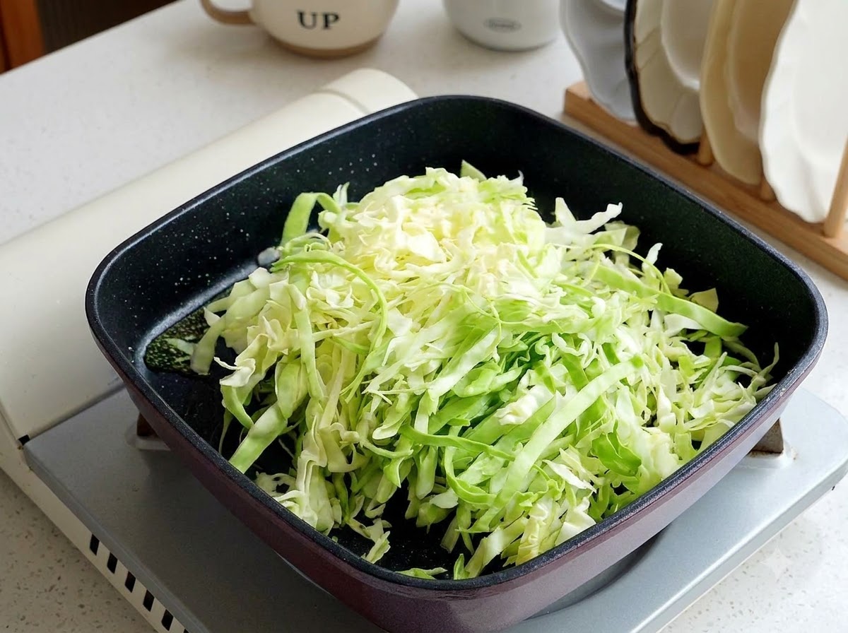Shredded cabbage being stir-fried in a black square pan over high heat.