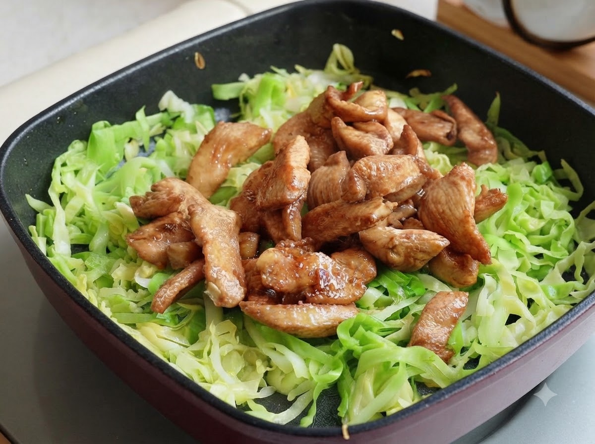 Cooked chicken breast strips placed on top of shredded cabbage in the pan, split into two sections.