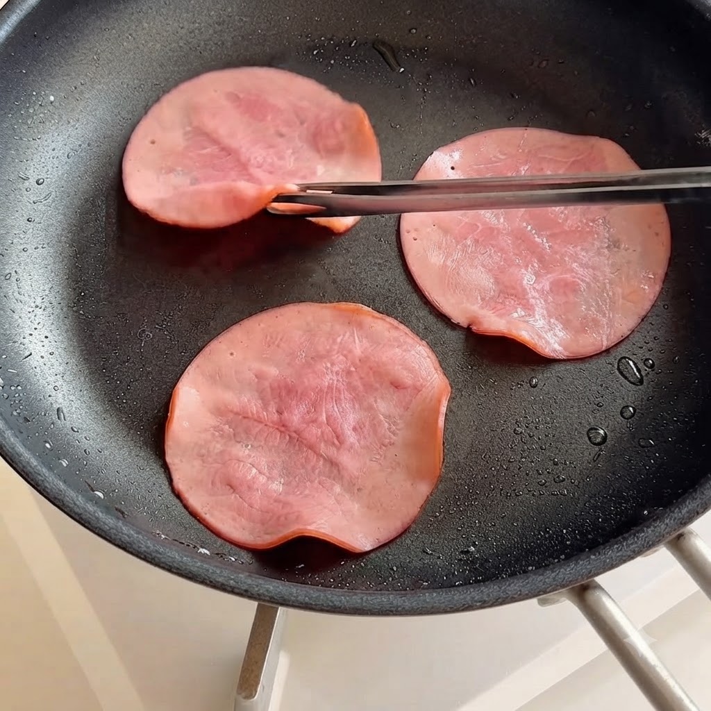 Ham slices being flipped in a frying pan using chopsticks.