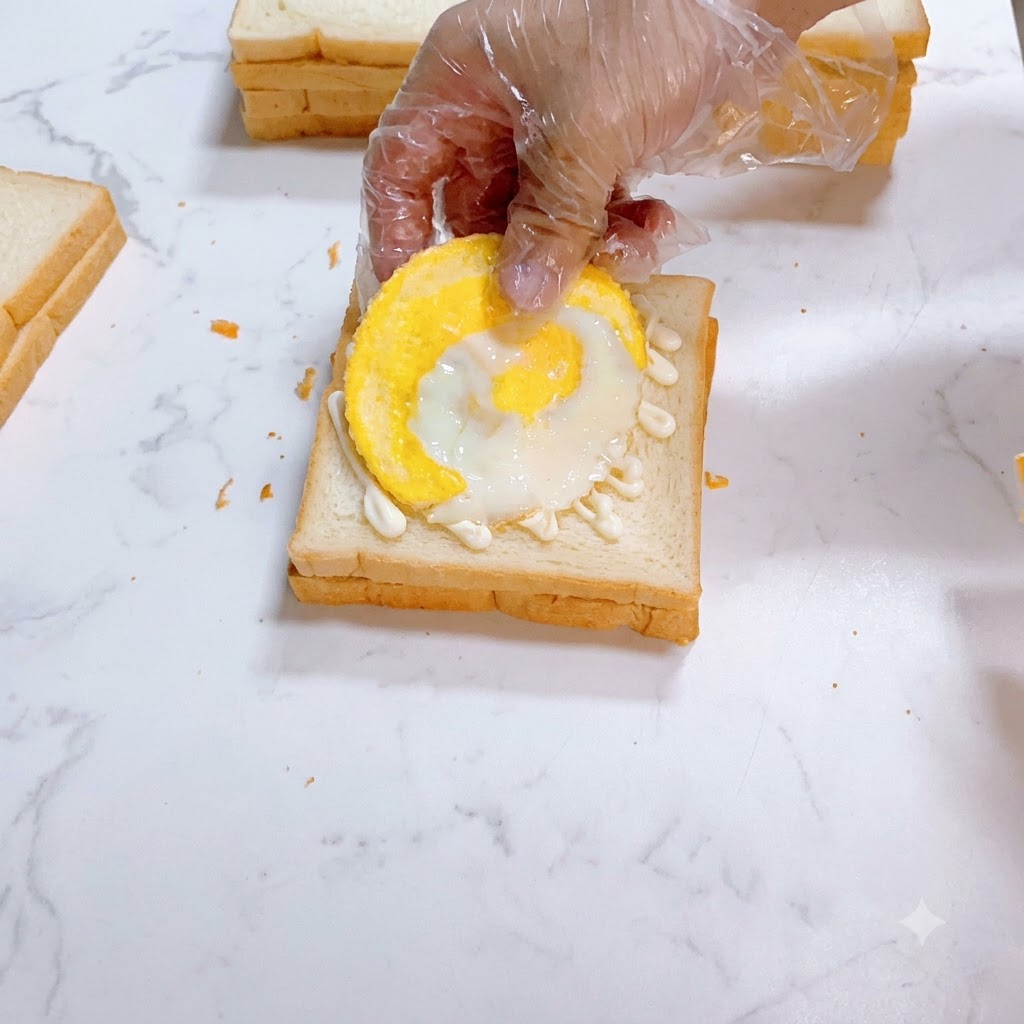A fried egg being carefully positioned on top of mayonnaise-spread white bread.