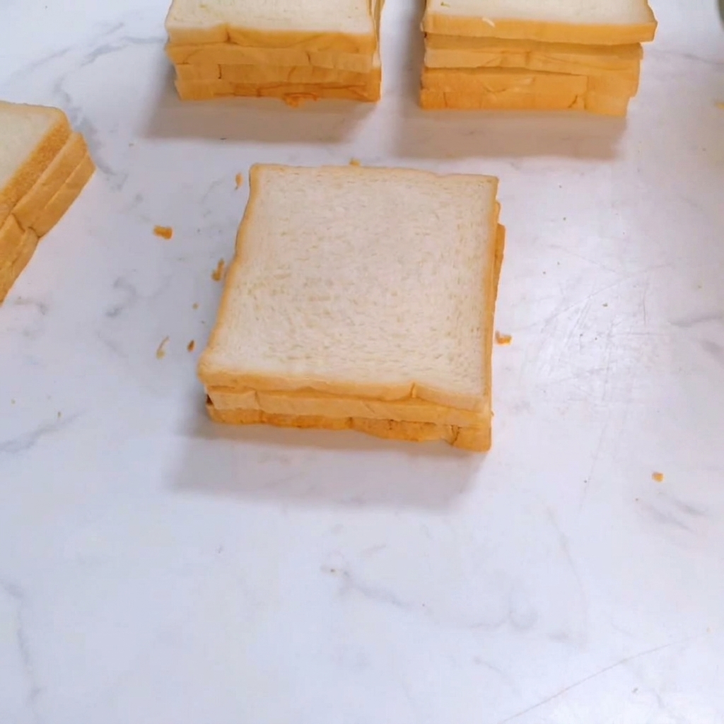 A third slice of square white bread being placed on top of the sandwich stack.