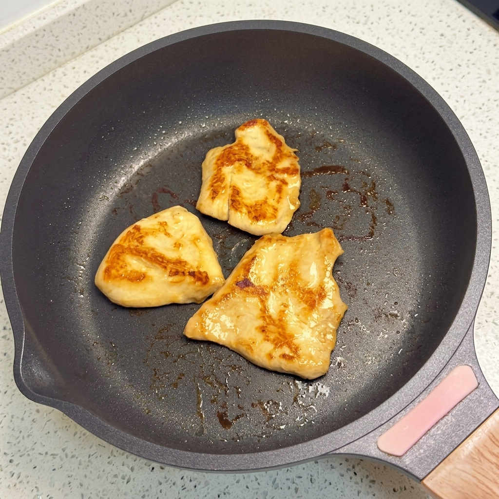 Chicken pieces frying in a flat-bottomed pan until golden brown.
