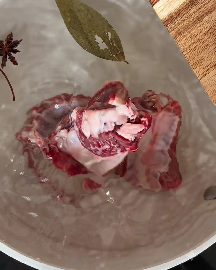Pork ribs simmering in a pot of water with star anise and a bay leaf floating on top.