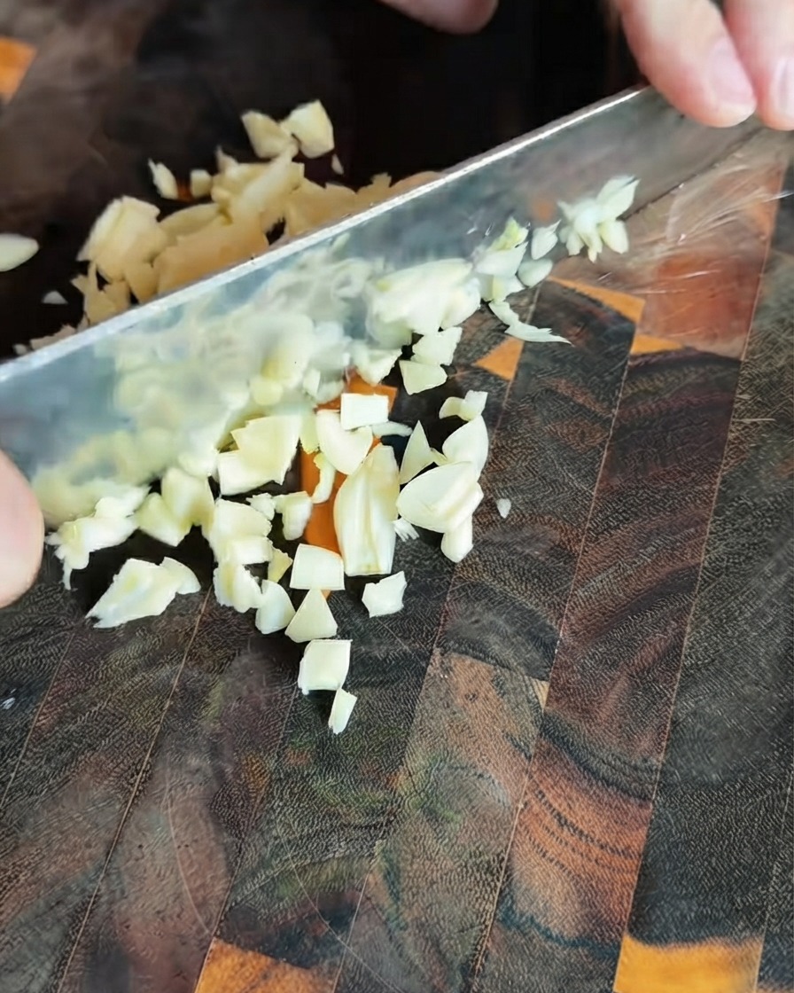 Freshly minced garlic pieces scattered on a dark wooden cutting board.