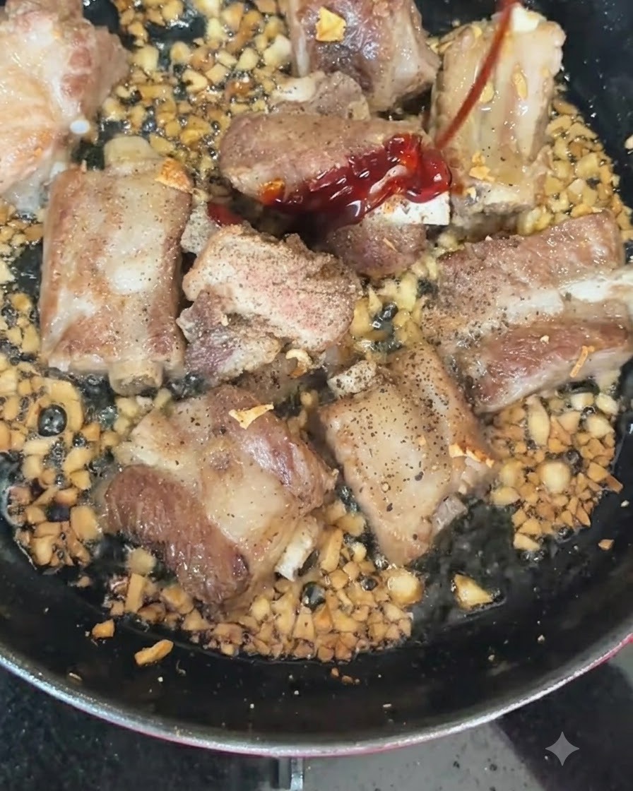 Red and green chilies being added to a hot pan containing searing pork ribs and chopped garlic.