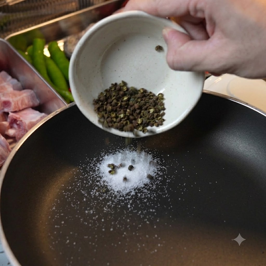 Green Sichuan peppercorns and coarse salt being poured into a black skillet for dry roasting.