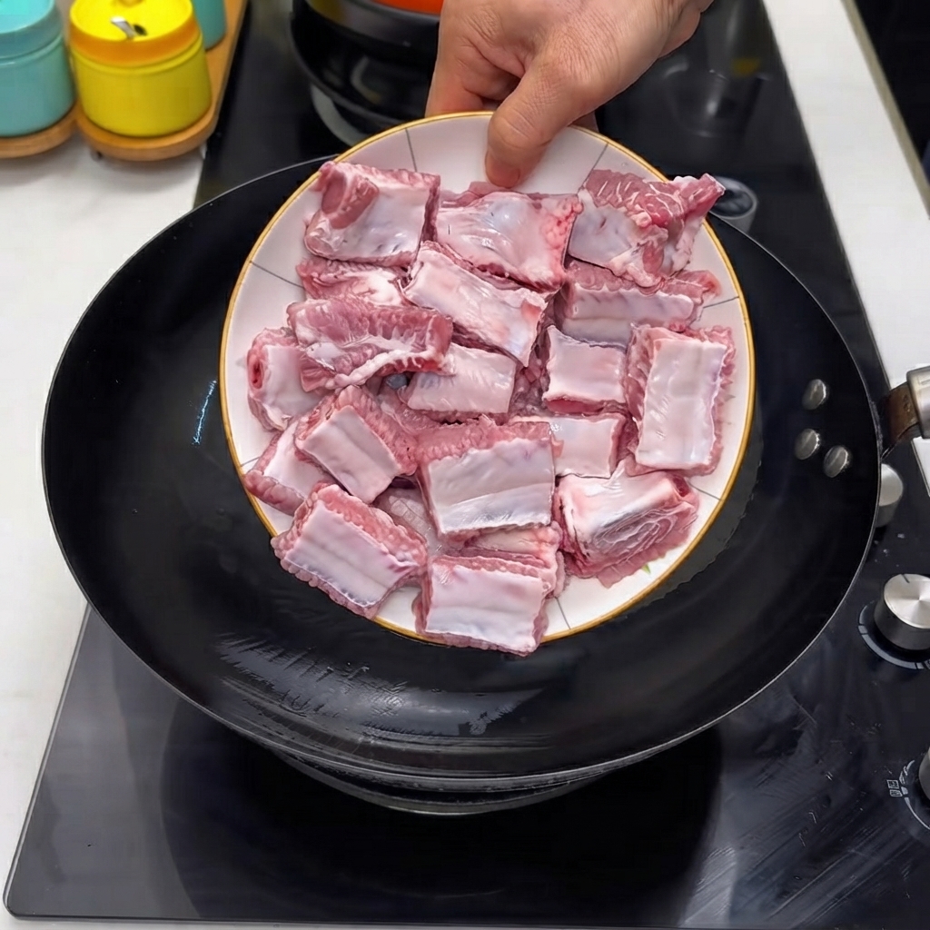 Raw pork ribs being poured from a white plate into a hot black wok.