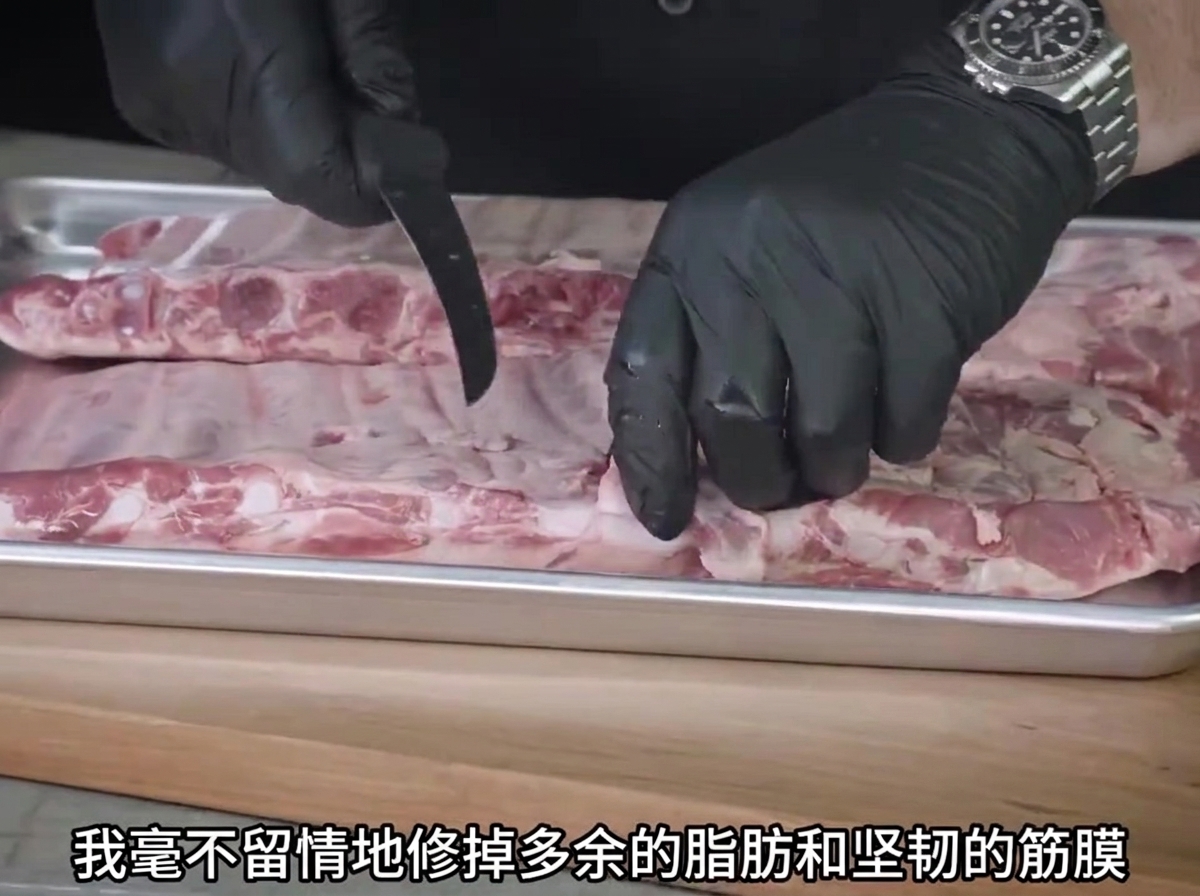 A pair of gloved hands using a knife to trim fat off raw spare ribs on a metal tray.