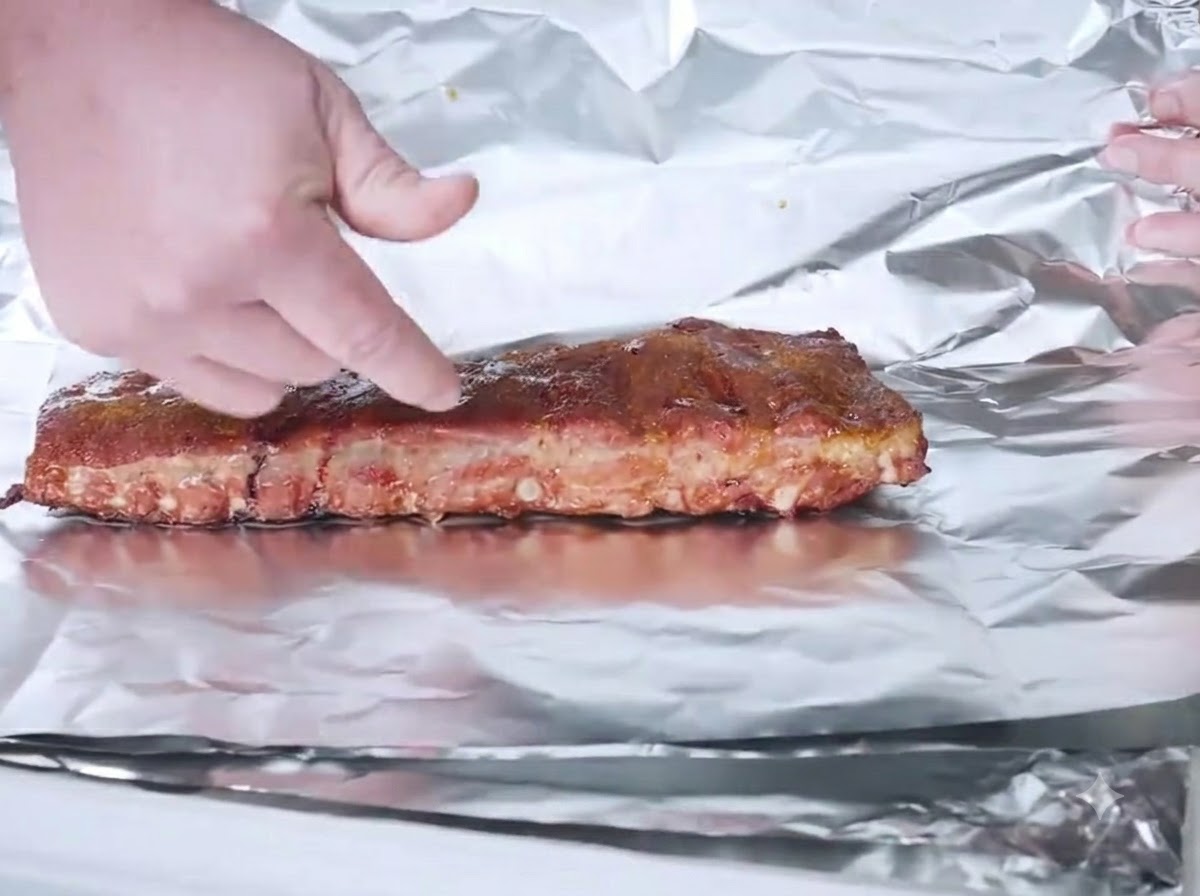 Smoked ribs placed on a sheet of aluminum foil ready to be wrapped.