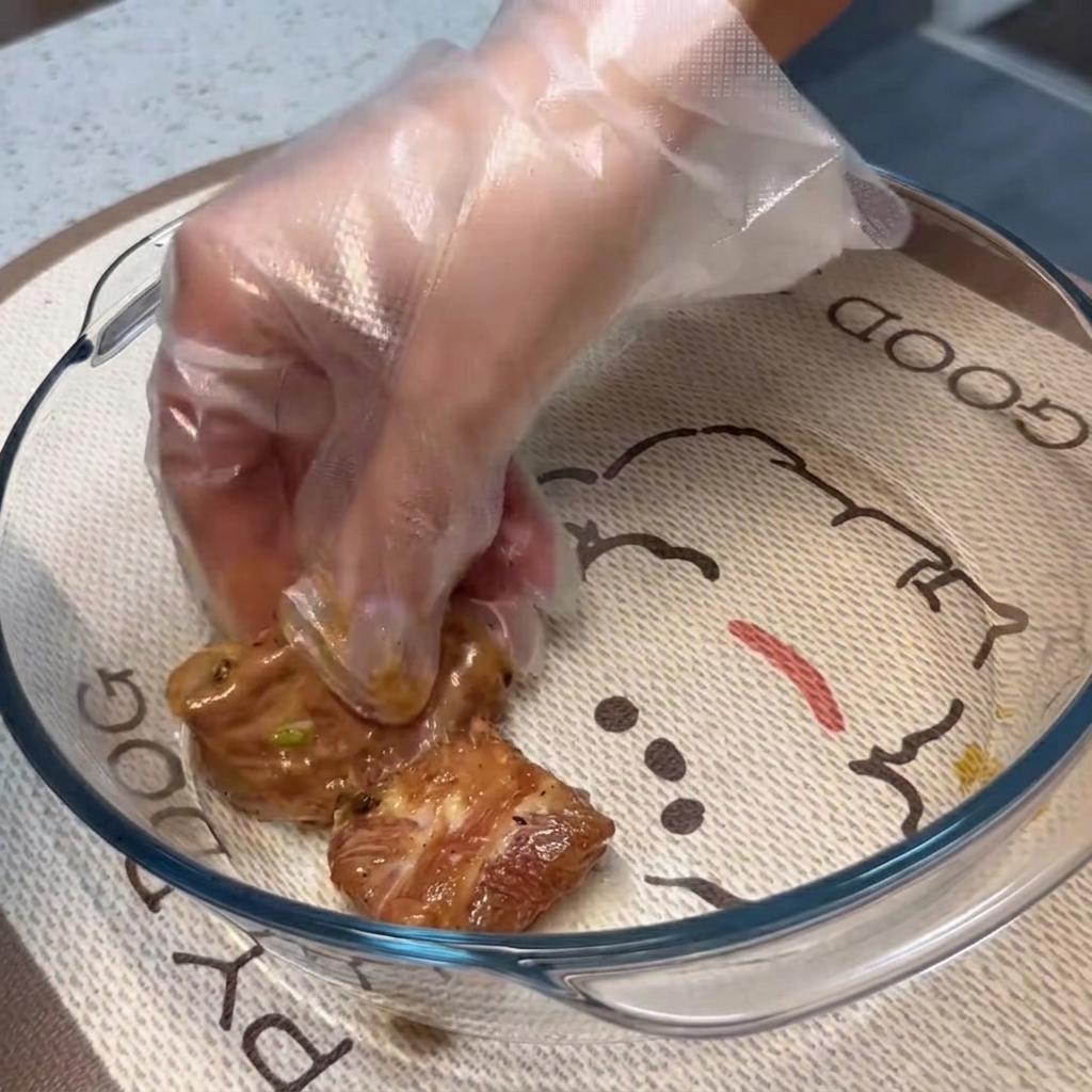 Marinated pork ribs being arranged in a flat, single layer inside a clear glass baking dish.