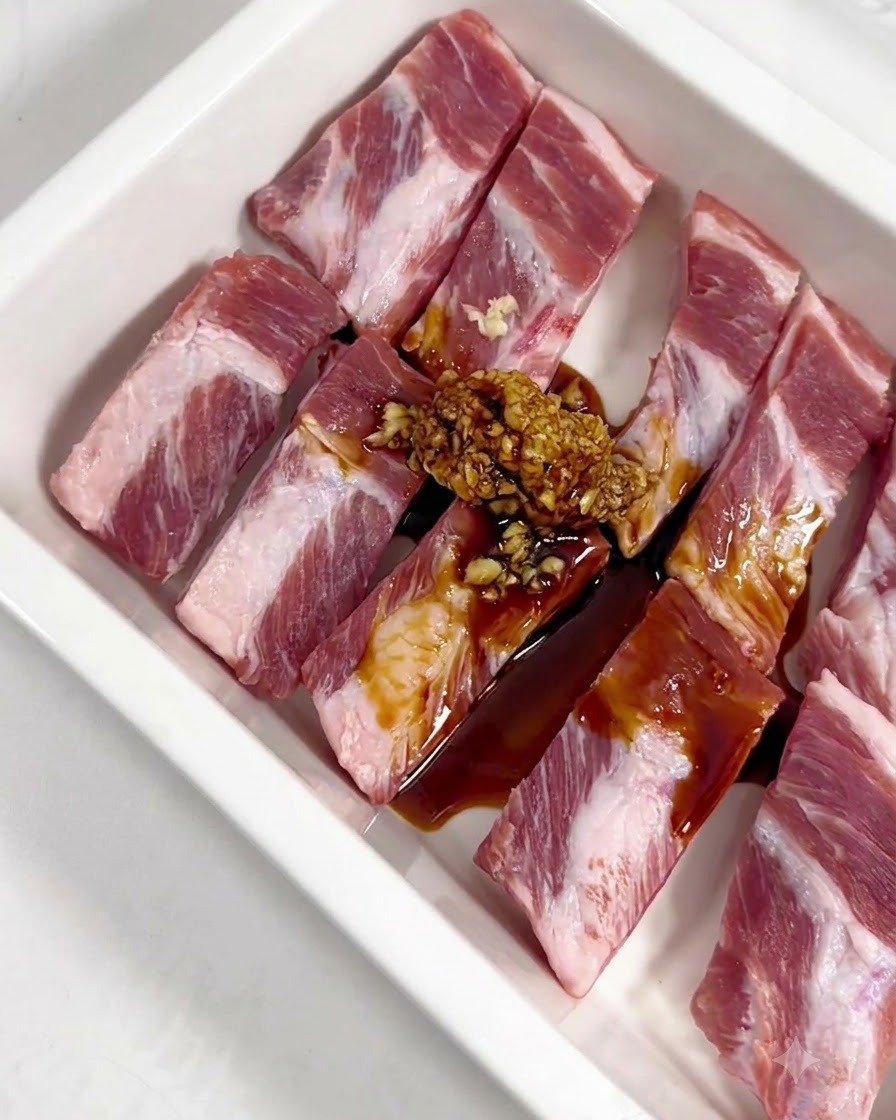 Minced garlic, soy sauce, oyster sauce, honey, and powder seasonings poured over raw pork ribs in a white tray.