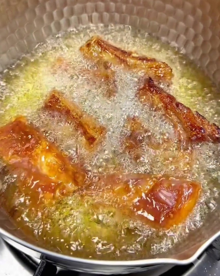 Pork ribs frying in hot oil over low heat with golden brown surfaces visible.