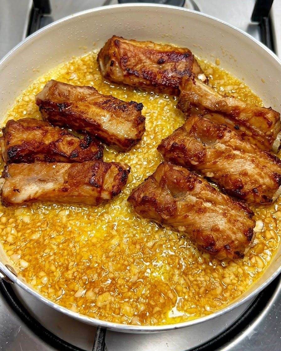 Golden-brown fried pork ribs laid out neatly inside a pan filled with bubbling garlic butter sauce.