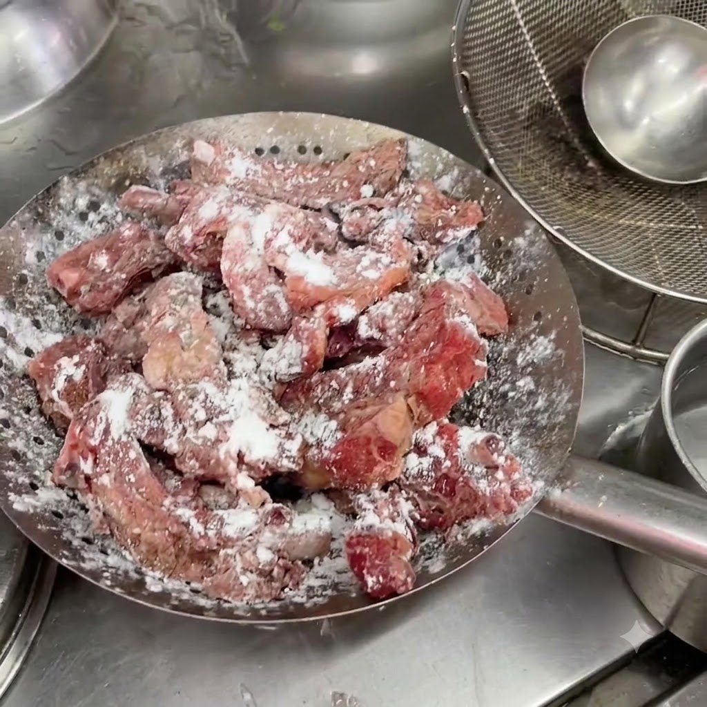 Marinated pork ribs resting inside a metal strainer with a visible white coating of starch.