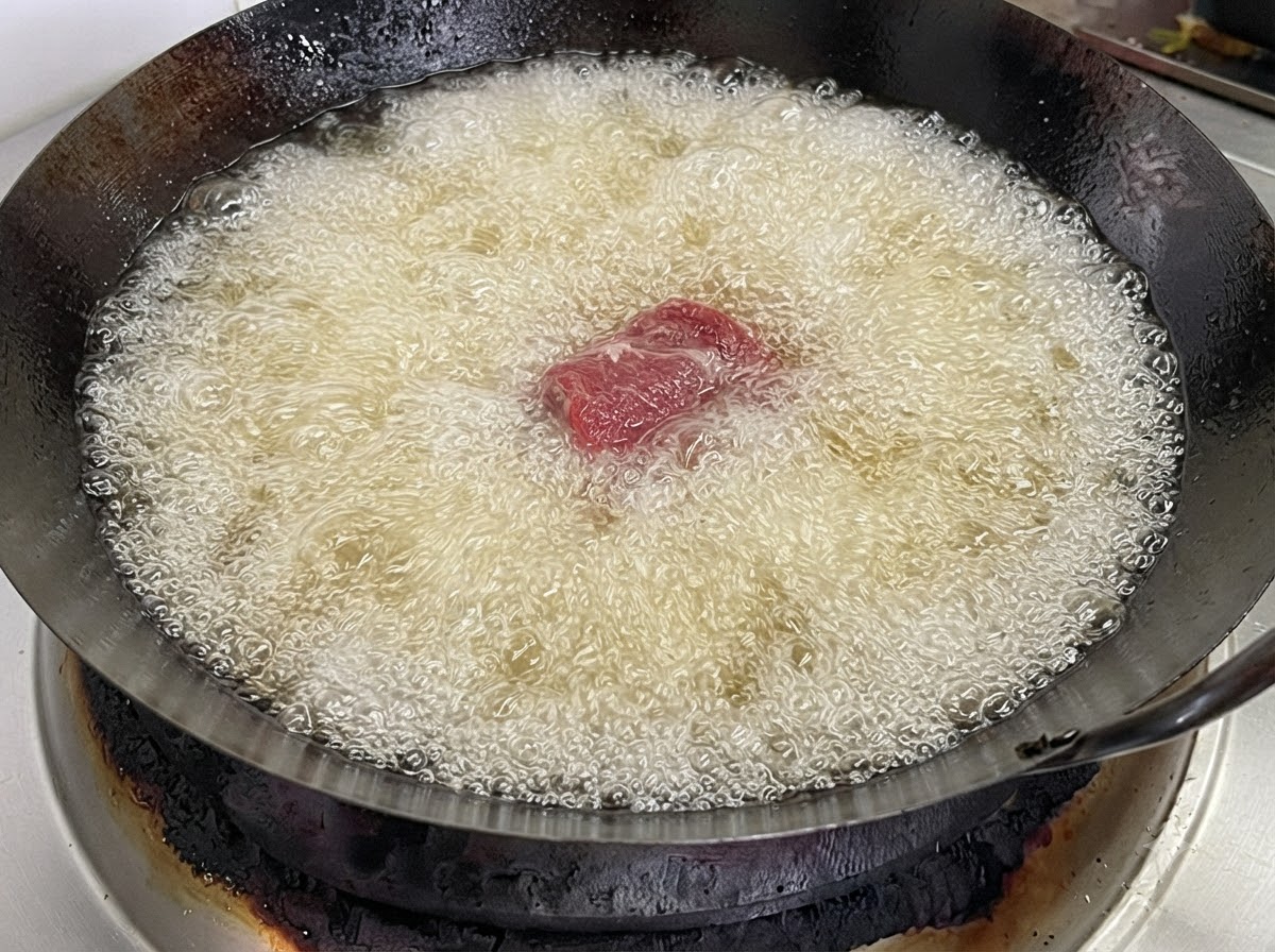 A single pork rib piece dropped into a wok filled with bubbling hot frying oil.