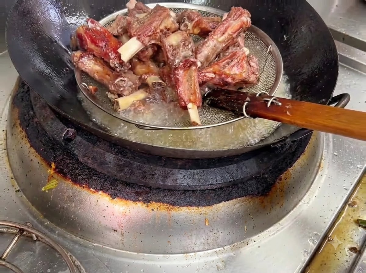 Fried pork ribs being lifted out of hot oil in a wire strainer basket.
