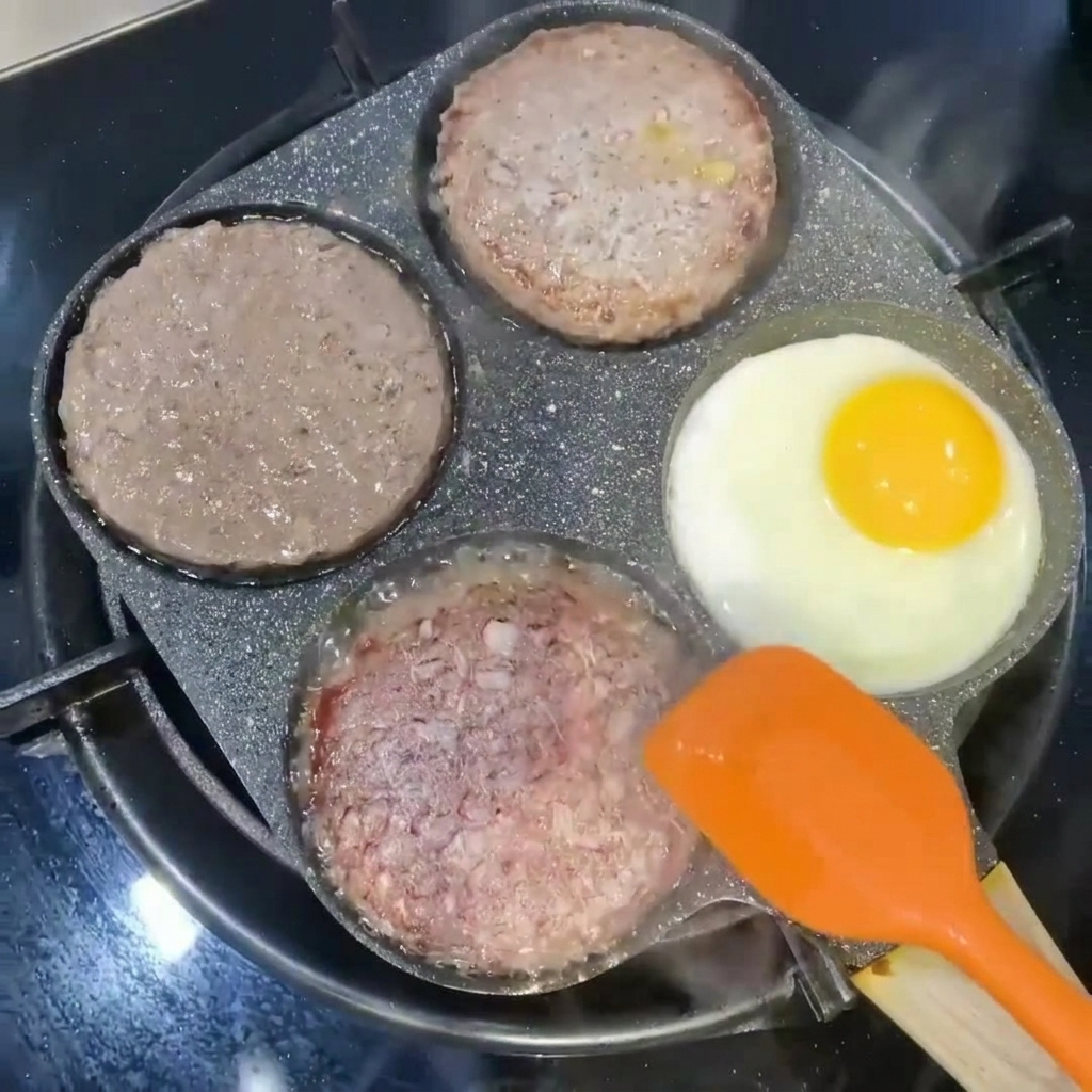 Burger patties being flipped with an orange spatula next to an egg frying in a pan section.