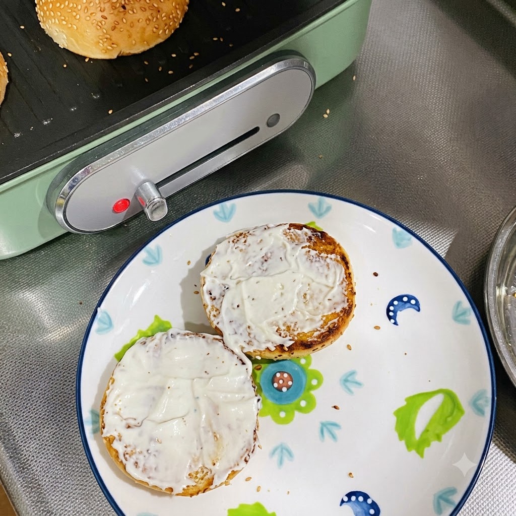 Two toasted bun halves coated with mayonnaise sitting on a decorated plate.