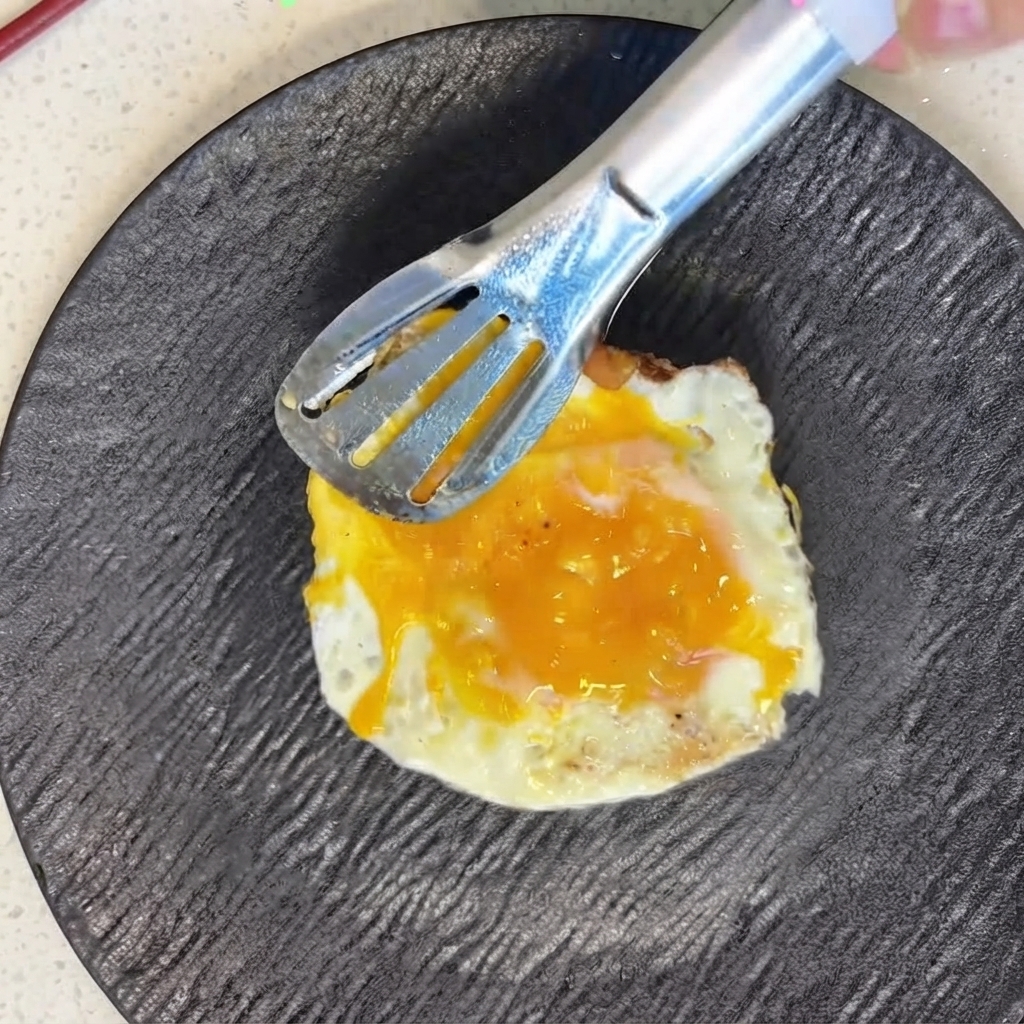 A freshly fried egg being carefully positioned on top of sliced tomatoes using metal tongs.
