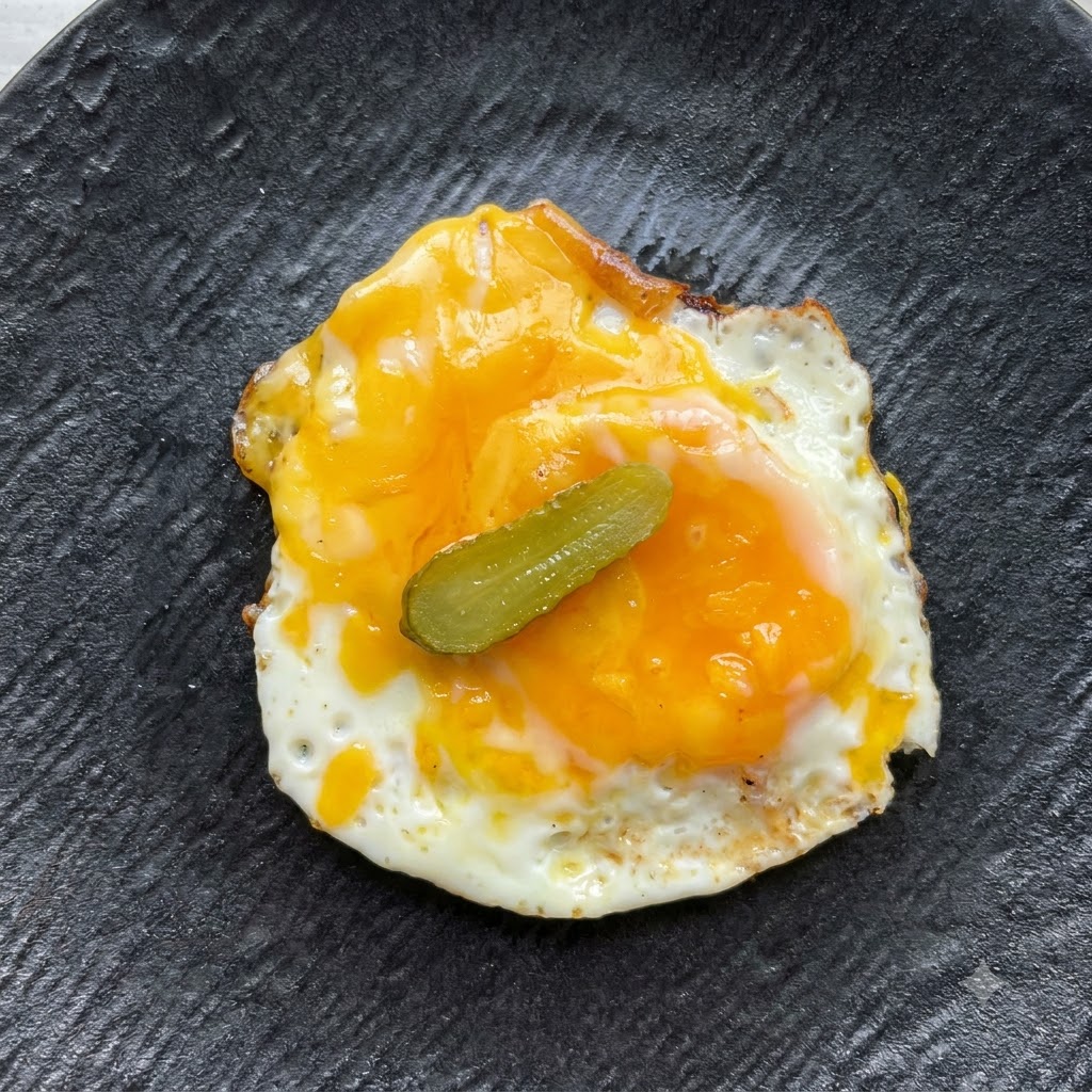A single small pickle slice placed centrally on top of the fried egg and cheese.