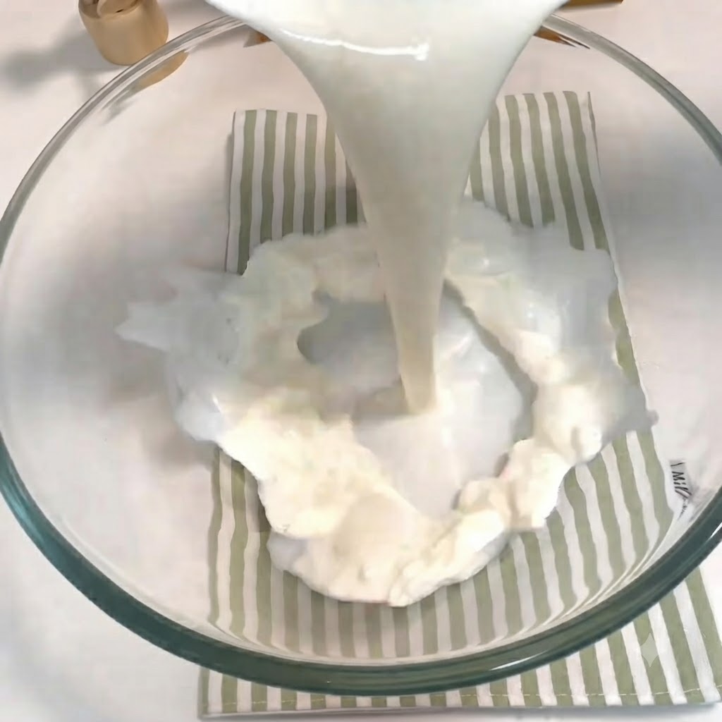 Milk, sugar, yeast, and an egg being poured and whisked together in a glass bowl.