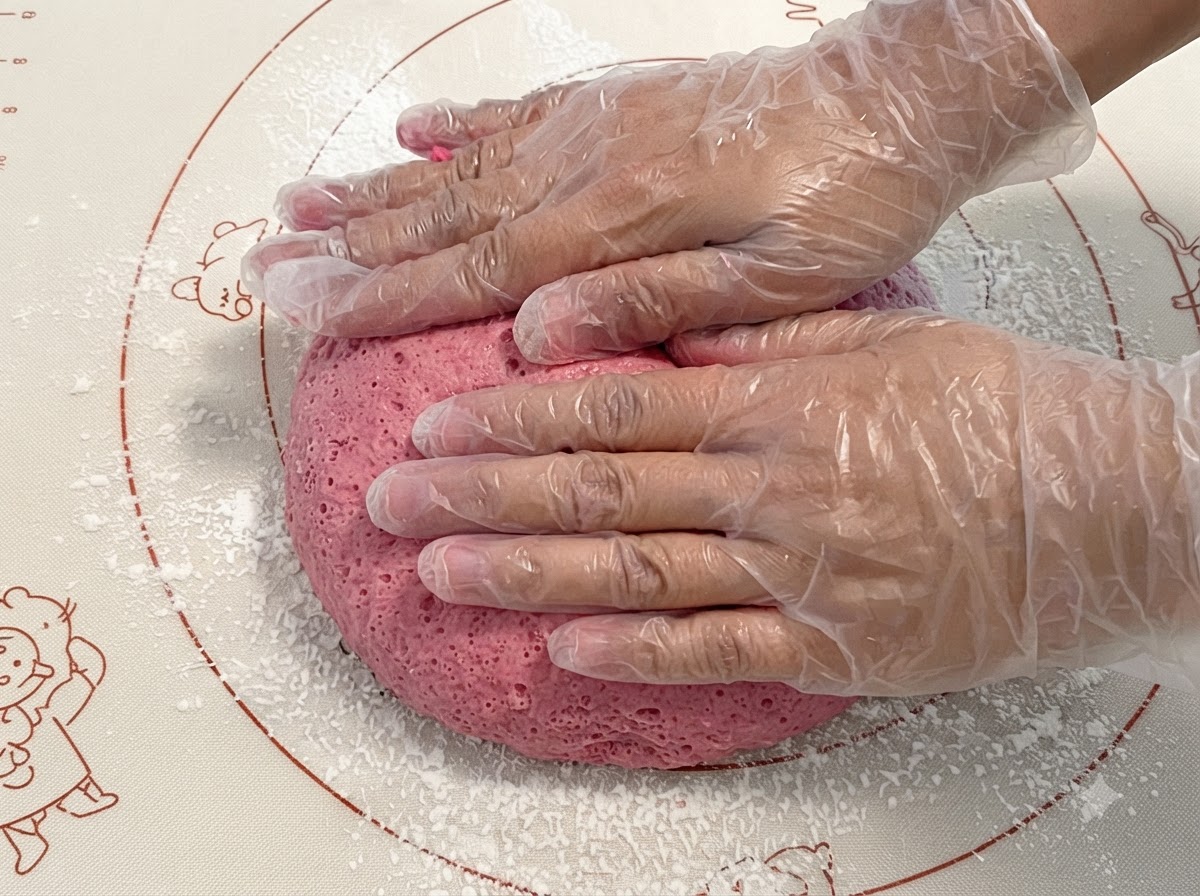 Fermented pink dough being pressed and kneaded on a silicone mat.