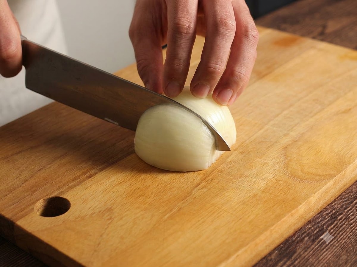 An onion being carefully chopped and minced on a wooden cutting board using a kitchen knife.