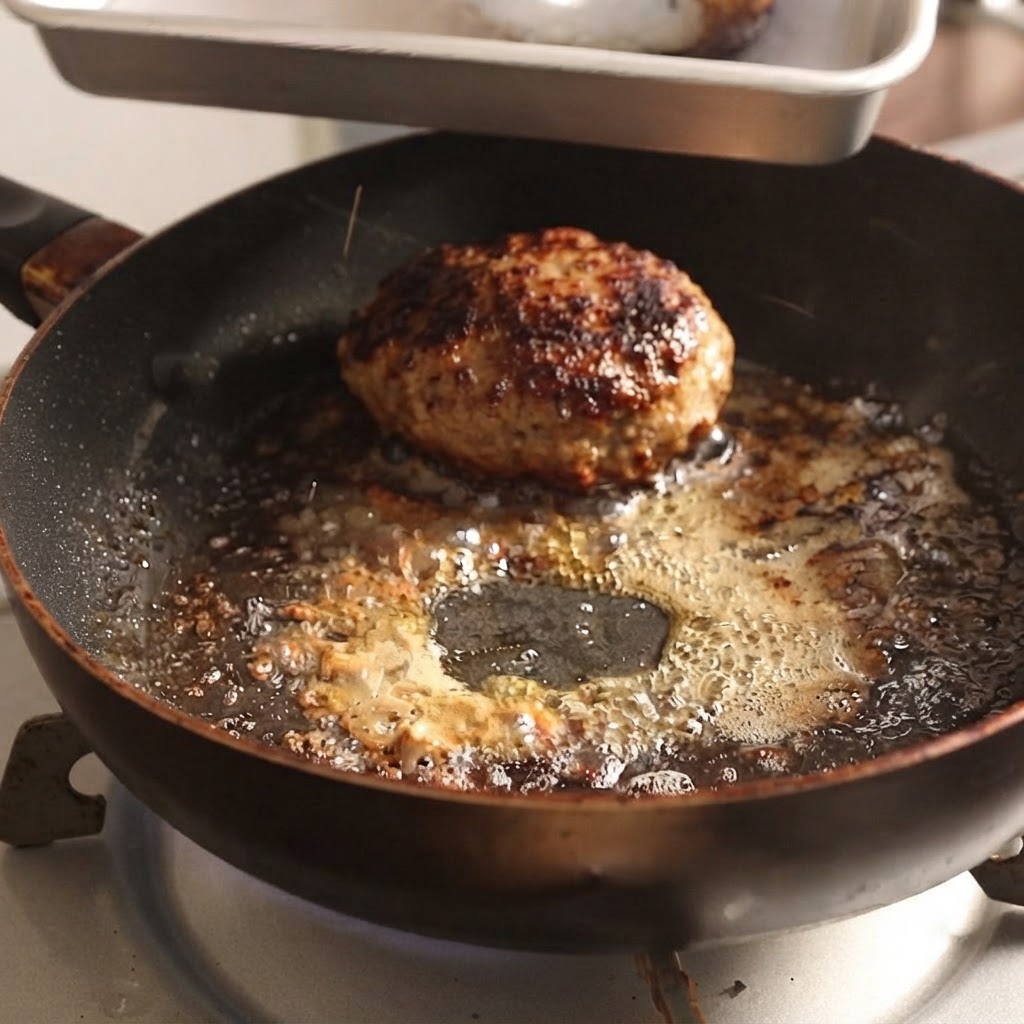 Hamburger patties being lifted out of a hot skillet using metal tongs.