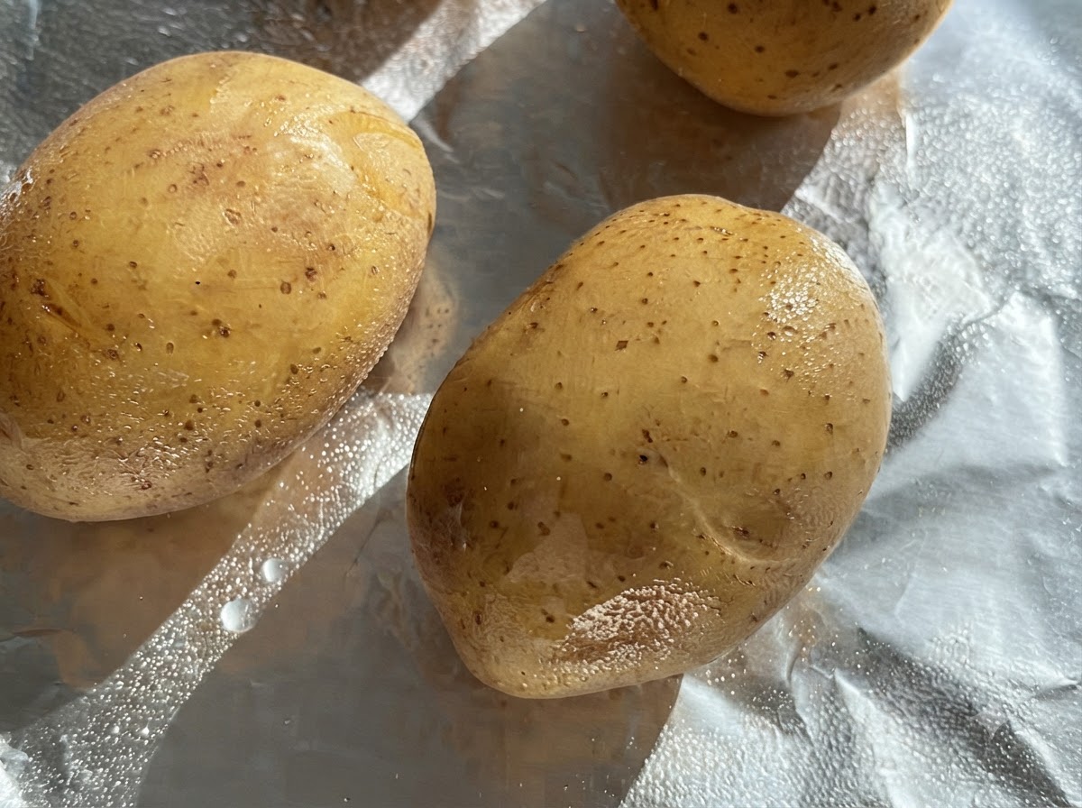Raw whole potatoes brushed with oil on a sheet of aluminum foil.